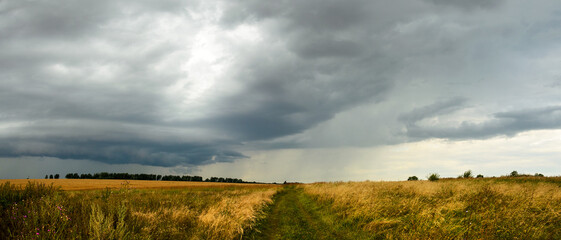 summer cloudy panoramic landscape with rural road passing through meadows and fields.ominous clouds 