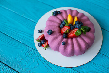 Poster - Pink cake garnished with slices of peach, strawberries, blueberries and mint leaves on a wooden blue background. Vegan dessert