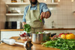 © Svitlana - Cropped shot of man, chef cook adding basil leaf to the pot with chopped vegetables while preparing healthy meal, soup in the kitchen. Cooking at home, Italian cuisine concept