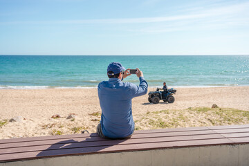 Wall Mural - Back view of man taking sea beach pictures by smart phone sunshine outdoors