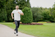 © muse studio - athletic man with dark hair running on a treadmill in a white t-shirt, doing sports in a green Park. excellent mood. cloudy day summer