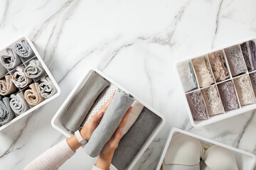 Woman hands neatly folding underwears and sorting in drawer organizers on white marble background.