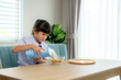 © ake1150 - Asian elementary school student girl in uniform eating breakfast cereals with milk in morning school routine for day in life getting ready for school.