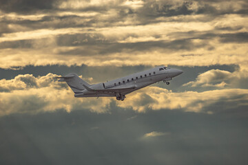 Wall Mural - White small private turbofan-powered twin-engine business jet airplane flying in air after takeoff from airport. Dramatic orange grey cloudy sky at sunset after rain storm, dynamic weather conditions.