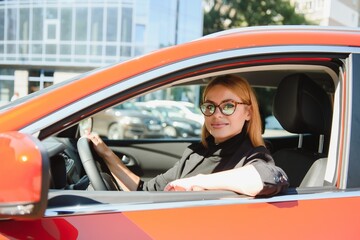 Wall Mural - successful businesswoman driving car through modern urban city with reflections of buildings