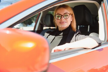 Wall Mural - successful businesswoman driving car through modern urban city with reflections of buildings