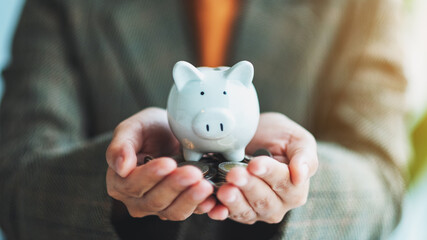 Closeup image of a woman holding piggy bank and coins in hands for saving money and financial concept