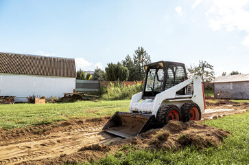 Wall Mural - A skid steer loader clears the site for construction. Land work by the territory improvement. Machine for work in confined areas. Small tractor with a bucket for moving soil and bulk materials.