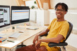 © AnnaStills - Portrait of African man sitting on chair in front of computer monitors and smiling at camera he working as a software developer