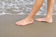 Close-up of child's legs walking on sand coast and sea water. Young girl legs on baltic sea beach. Teenager legs near sea line.