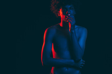 Black man. Neon light portrait. Tired african guy with shirtless torso in blue red glow touching face. Isolated on dark copy space. Confused feelings. Ethnic problems. No racism