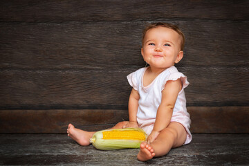 baby girl sits on the wooden background and chews corn silk