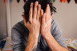 © J Danielle Photography/Stocksy - A man with tattoos sitting on a bed hiding his face in his hands out of frustration.