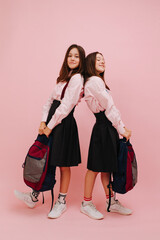 Happy little twin schoolgirls posing with their backpacks, holding them in hands