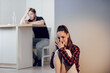 © Olha - Victim of domestic violence. Young scared woman with bruises on face complains to girlfriend on cell phone sitting on the floor in the kitchen. Her husband is sitting behind and drinking alcohol