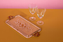Two Vintage Classsic Martini Cocktail Glasses Standing Next To A Glass Serving Plate With Flowers On A Brown Surface And A Pink Background. Clean Minimalistic Elegant Style