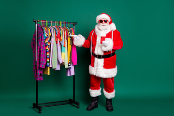 Full length photo of santa claus noel tradition x-mas designer point index finger wardrobe garment shopper buyer purchase wear red costume headwear isolated over green color background