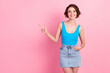 Photo of lovely pretty confident young lady directing finger empty space shiny smiling make perfect proposition wear denim mini skirt blue tank-top isolated pink color background
