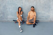 © puhhha - Skateboarding. Couple In Casual Outfit Sitting On Skateboards Against Concrete Wall At Skatepark. Urban Sport As Hobby Of Active Guys And Girls. Skater Subculture And Summer Activity As Lifestyle.