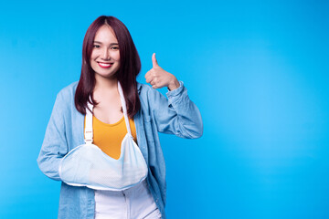 Patient young woman wearing soft splint armband form accident showing thumb up while standing on blue isolated on blue background. Insurance accident concept.