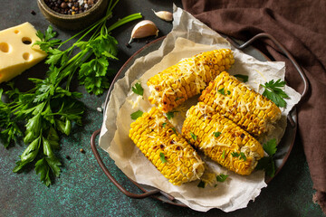 Summer vegan dinner or snacks. Grilled corn with garlic butter, served with cheese on a dark stone table top.