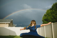 Little Girl Spinning In Her Backyard With A Rainbow Overhead
