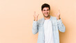 © Asier - Young man isolated on beige background showing a horns gesture as a revolution concept.