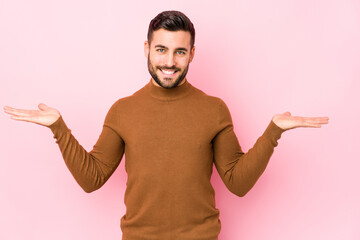 Young caucasian man against a pink background isolated makes scale with arms, feels happy and confident.