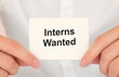 © Sinfebeth - Man's hands take a card with words Interns Wanted, finance and business concept.