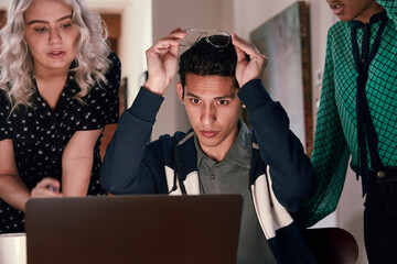Group of young co-workers gathered around laptop computer looking at screen discussing project  