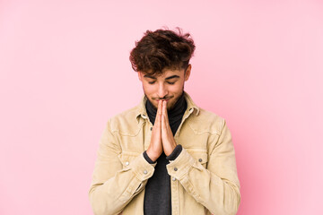 Wall Mural - Young arabian man posing in a background isolated holding hands in pray near mouth, feels confident.