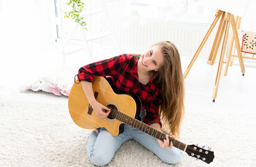 Wall Mural - Cute girl with long loose hair playing guitar in light room