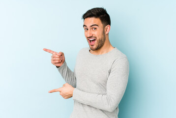 Young caucasian man isolated on blue background pointing with forefingers to a copy space, expressing excitement and desire.