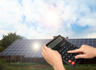 Woman using calculator against house with installed solar panels. Renewable energy and money saving