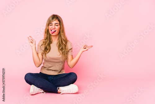 Cuadros en Lienzo Young blonde caucasian woman sitting on a pink studio showing rock gesture with
