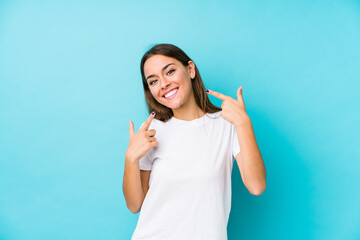 Wall Mural - Young caucasian woman  isolated smiles, pointing fingers at mouth.