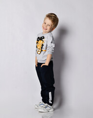 Wall Mural - Laughing blond kid boy in black pants and shirt with lion print stands side to camera with hands in pockets