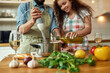 © Svitlana - Cropped shot of man, chef cook using hand blender while preparing a meal. Young woman, girlfriend in apron pouring olive oil in the pot, helping him in the kitchen