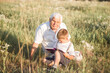 © Maria - Mid shot of grandfather and his grandson while reading a book together in meadow Small boy making first steps in read.