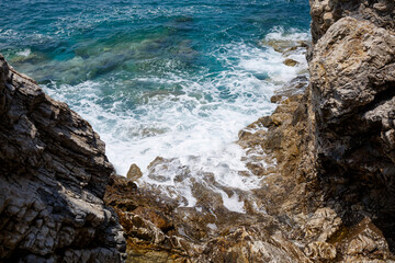 Wonderful views of the blue Mediterranean Sea. Sunny rocks, waves with foam and splashing water. The wave crashes into the rocks on the shore