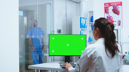 Nurse in blue uniform entering in hospital cabinet while medic is using computer with green screen mock-up.