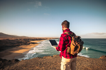 Wall Mural - Digital nomad people smart working concept with standing man work with laptop computer and internet connection roaming in wild outdoor place with amazing beach view - travel lifestyle off grid