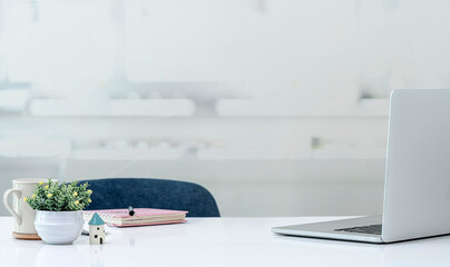 Home office concept. Mockup laptop computer with supplies on white top table in white room.