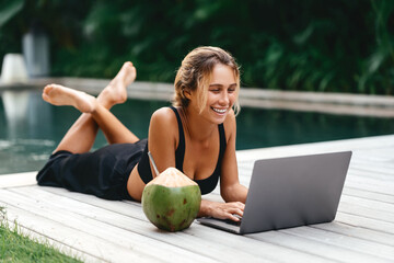 Attractive young female sitting in the swimming pool and working on a laptop