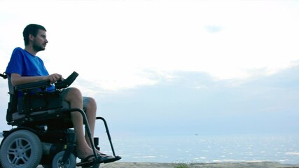 Wall Mural - Man on wheelchair near sea looking at sunset.