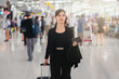 © shine - Asian businesswoman walking with a luggage at airport terminal and airport terminal blurred crowd of travelling people on the background.