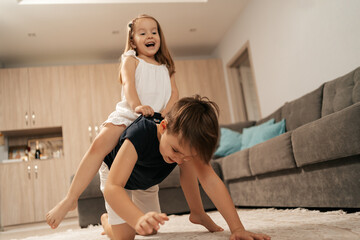 cheerful boy and girl playing at home. brother carries on his back, his happy sister