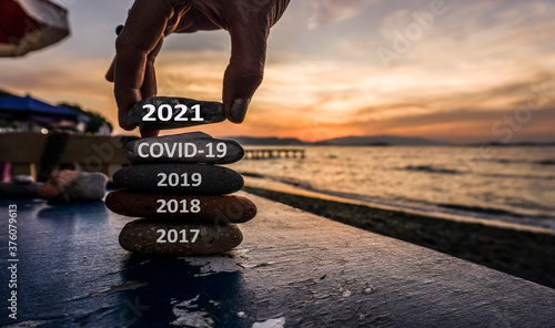 New Year 2021 is coming concept. Covid year 2020 to 2021 background. Positive turn of old year. Happy new year 2021 replace corona. New hopes, excitement with 2021. Man adding stone to pebble tower
