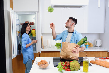 Beautiful young couple unpacking together fresh products from market in the kitchen.The man throws up the cabbage.