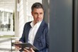 © nyul - Confident elegant older businessman in suit standing and working with business tablet computer in office atrium.